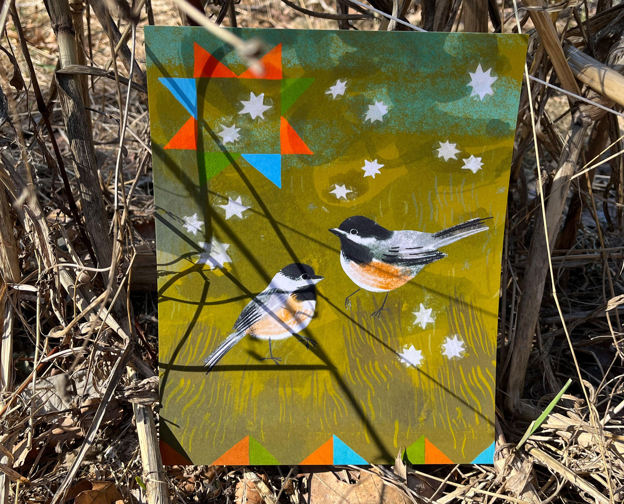 Photo of a print of a painting of twochickadees on a green background under a quilt square